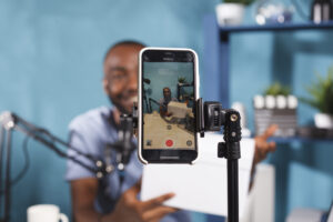 blogger making giveaway while live streaming smartphone screen closeup web content creator announcing contest showing prize gift using mobile phone tripod video recording scaled 1